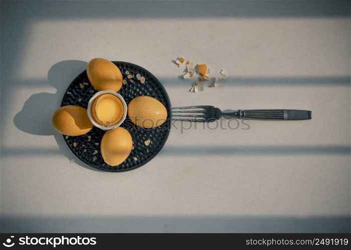 Composition of Broken fresh chicken egg (Hen egg) put at the middle of the fresh eggs with brown eggshell and Black antique silver fork on white table. Natural organic healthy food concept, Top view, Copy space. Selective focus.