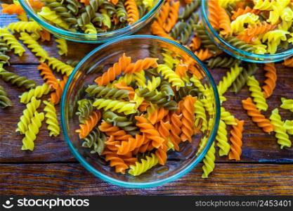 Composition of raw pasta uncooked tricolore fusilli, pasta twist shape. Close up and selective focus on colorful fusilli pasta. Fusilli pasta in bowl.