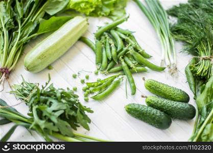 Composition on a white background of green organic vegetarian products: green leafy vegetables, beans, zucchini, garlic, onions, cucumbers, peppers, spinach. view from above. Green food. Composition on a dark background of green organic vegetarian products