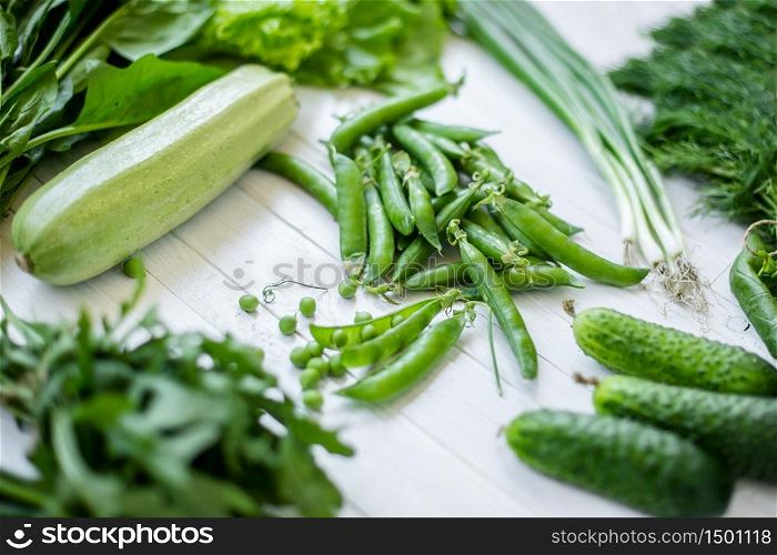 Composition on a white background of green organic vegetarian products: green leafy vegetables, beans, zucchini, garlic, onions, cucumbers, peppers, spinach. view from above. Green food. Composition on a dark background of green organic vegetarian products