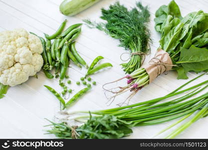 Composition on a white background of green organic vegetarian products: green leafy vegetables, beans, zucchini, garlic, onions, cucumbers, peppers, spinach. view from above. Green food. Composition on a dark background of green organic vegetarian products