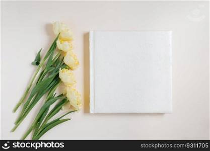 Composition with a wedding or family photo album, a bouquet of flowers of yellow tulips on a light background. Flat lay, top view still life.