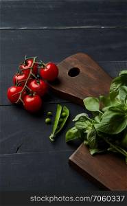 Composition with assorted raw organic vegetables and hearbs on black wooden background.. Board with fresh basil, tomatoes and green beans on wooden background