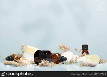 Composition with bottles of essential oils, facial serum, creams on table with stones and flowers on blue background. Natural cosmetics. Bio organic spa and beauty products. Eco-friendly zero waste packaging