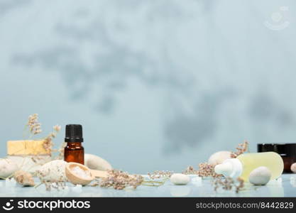 Composition with bottles of essential oils, facial serum, creams on table with stones and flowers on blue background. Natural cosmetics. Bio organic spa and beauty products. Eco-friendly zero waste packaging