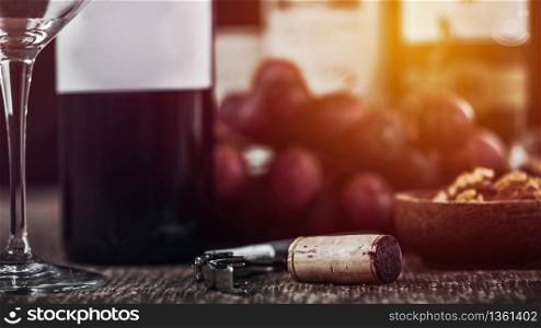 Composition with corkscrew bottle opener, empty wine glass, nuts in wooden bowl and fresh grapes in background.