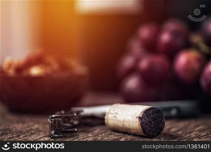 Composition with corkscrew bottle opener, nuts in wooden bowl and fresh grapes in background.
