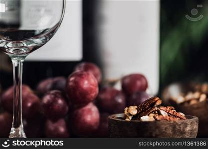 Composition with empty wine glass, different bottles of red wine, nuts in wooden bowl and fresh grapes. Close up.