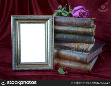 Composition with photo frame, stack of antique books and a dry rose on a background of red velvet