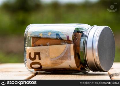 Composition with saving money banknotes in a glass jar. Concept of investing and keeping money, close up isolated.