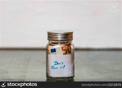Composition with saving money banknotes in a glass jar with text Do not touch it. Concept of investing and keeping money, close up isolated.