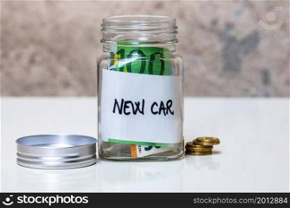 Composition with saving money banknotes in a glass jar with text new car .Concept of investing and keeping money, close up isolated.