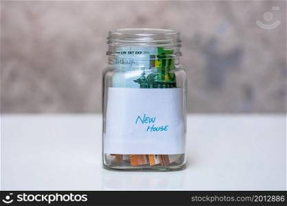 Composition with saving money banknotes in a glass jar with text new house. Concept of investing and keeping money, close up isolated.