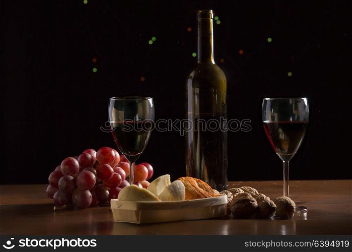 Composition with wine, cheese, nuts and grape on wooden table, on black background