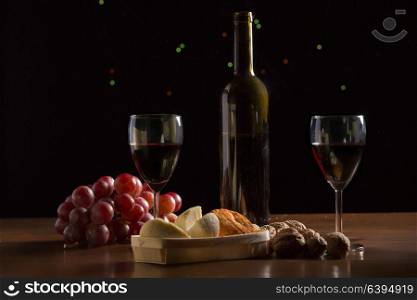 Composition with wine, cheese, nuts and grape on wooden table, on black background