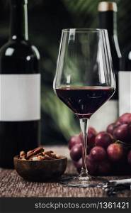 Composition with wine glass, different bottles of red wine, nuts in wooden bowl and fresh grapes