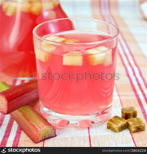 Compote from rhubarb in a glass and pitcher, rhubarb stalks, sugar on background tablecloth