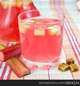 Compote from rhubarb in a glass and pitcher, rhubarb stalks, sugar on background tablecloth