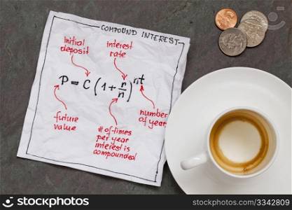 compound interest equation on a cocktail napkin with empty coffee cup and coins on a slate stone table