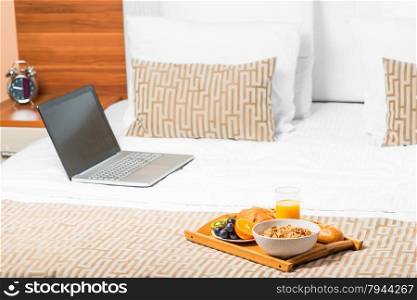 computer and a tray of food on the bed in the bedroom