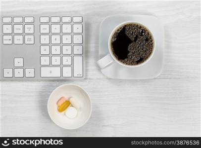 Computer keyboard with a cup of hot coffee and daily supplements on white rustic wood. High angled shot in horizontal format.