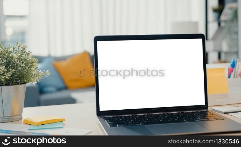 Computer laptop with blank white screen mock up display for advertising text on desk in living room at modern house. Chroma key technology, Marketing design concept.