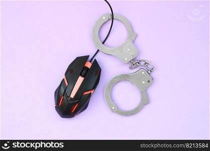 Computer mouse in a red color is chained in handcuffs on the background of purple color. The concept of combating computer crime, hackers and piracy. Flat lay top view. Creative concept of combating computer crime, hackers and piracy