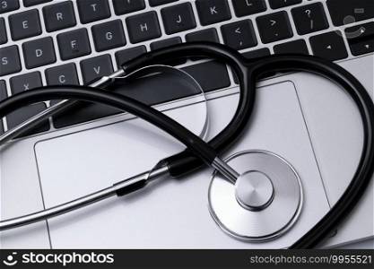 Computer repair, IT industry or modern medical service concept - top view of a black stainless stethoscope on a laptop keyboard.
