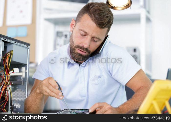 computer repairman on the phone while repairing desktop computer