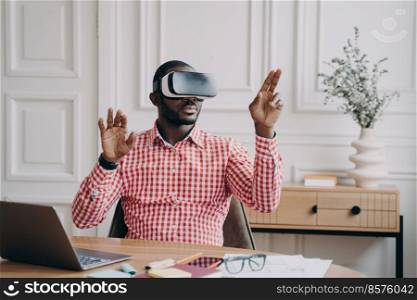 Concentrated Afro American businessman using VR headset, experiencing virtual reality while playing video game. Afro male pointing fingers up seemingly interacting with objects from cyber space world. Concentrated Afro american businessman using VR headset, experiencing virtual reality playing game