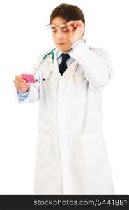 Concentrated doctor raising eyeglasses and reading name of drug isolated on white&#xA;