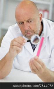 concentrated senior scientist chemists hold magnifying glass in lab