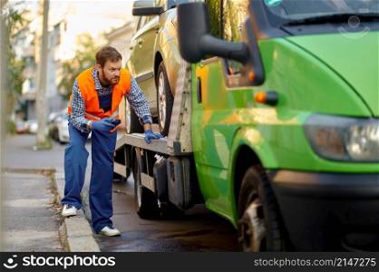 Concentrated tow truck worker in uniform checking car loading accuracy. Preparation for evacuation. Tow truck worker checking car loading accuracy