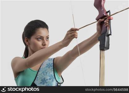 Concentrated woman practicing archery against gray background