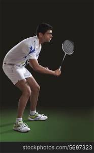Concentrated young man in sportswear playing badminton over black background