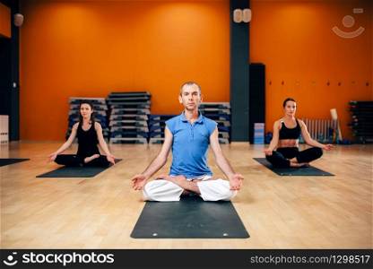 Concentration training, female group with instructor sitting in yoga pose, fat burn exercise, workout in gym. Yogi indoor