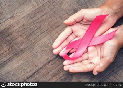 concept healthcare and medicine. hand holding pink ribbon on wood. breast cancer awareness. sign of hope