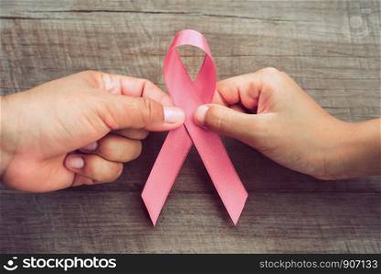 concept healthcare and medicine. two hand holding pink ribbon on wood. breast cancer awareness. sign of hope