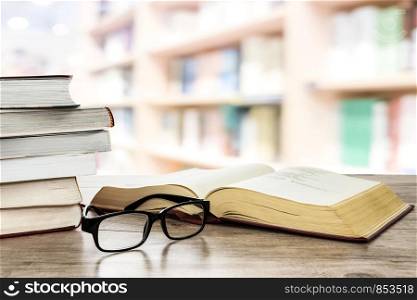 Concept image of education and learning - stocks of books next to open book and eyeglasses on a desk in the library.