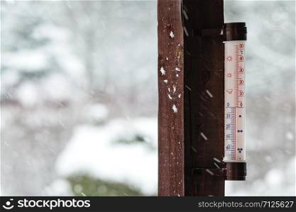 Concept image of winter coming - thermometer outside the house indicates below zero and it is snowing heavily.