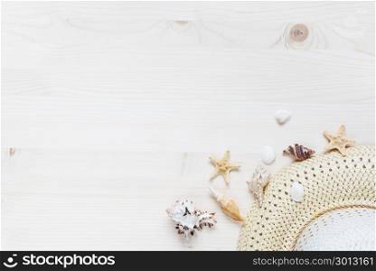 Concept of a beach holiday: straw hat and seashells are on a light wooden surface. Top view, flat lay