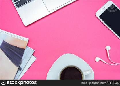 Concept of a creative workplace for a modern woman - a laptop, a smartphone with headphones, fashion catalogs and coffee on a pink desk (top view and copy space)