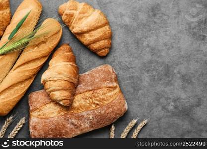 Concept of a local bakery, fresh pastries - baguette, croissant and ciabatta. Baked wheat bread lies on a gray table. Various types of freshly baked bread. Bread layout with copy space