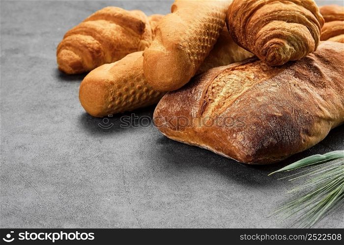 Concept of a local bakery, fresh pastries - baguette, croissant and ciabatta. Baked wheat bread lies on a gray table. Various types of freshly baked bread. Closeup with copy space