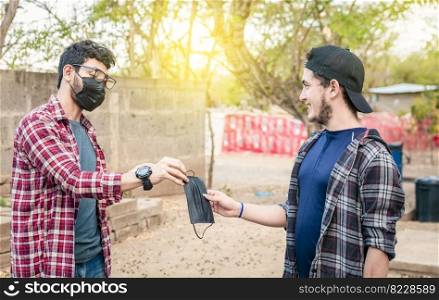 Concept of a person giving a surgical mask, Two young people giving each other a surgical mask, Side view of young man giving a surgical mask to another person outdoor