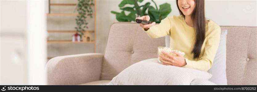 Concept of activity in home, Young woman holds remote control to changing channel and eats popcorn.
