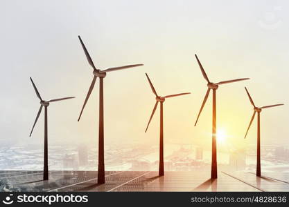 Concept of alternative electricity power with windmills on sunset background. Alternative wind energy