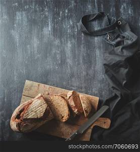 Concept of baking and cooking background. Sliced dark bread. Bread with a knife on a wooden board on a dark background. Sliced bread on wooden board