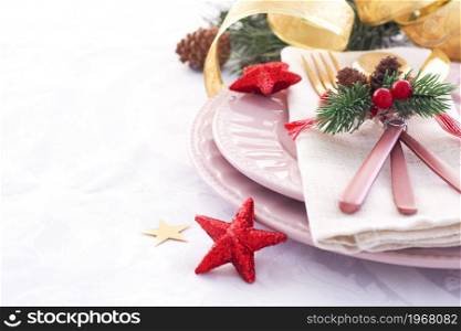 concept of christmas table setting. two pink plates and pink and gold cutlery with decor on a linen napkin. fir branches, cones and stars.