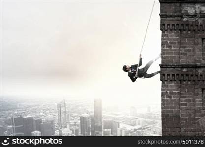 Concept of competition with businessman climbing office building with rope. Reach the top